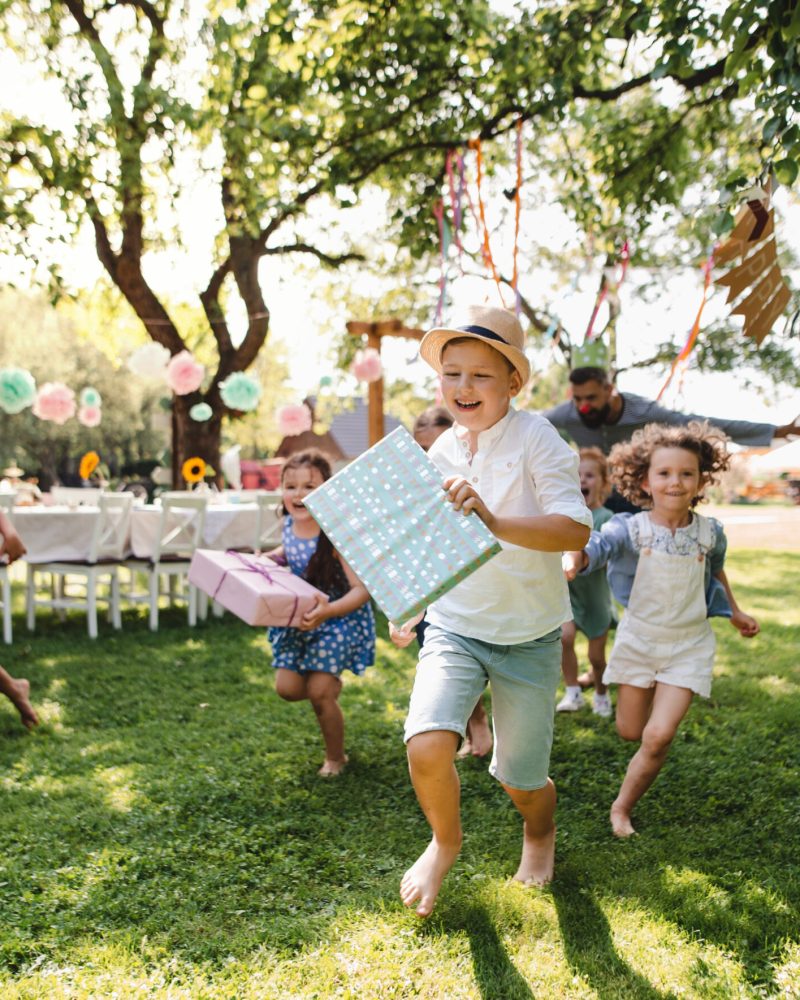 Small children ruunning with present outdoors in garden on birthday party, playing.